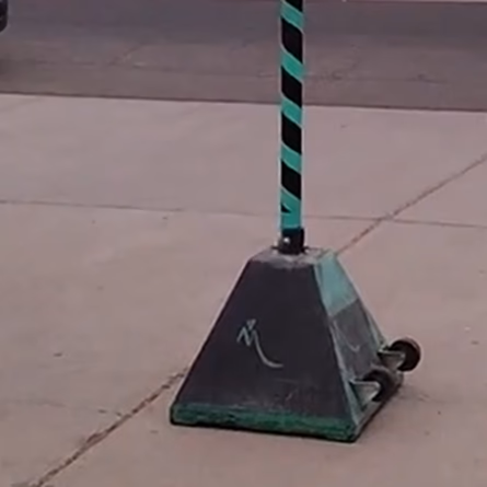 The TetherKing pole, striped black and green, seated in its black commercial sign base on a concrete driveway